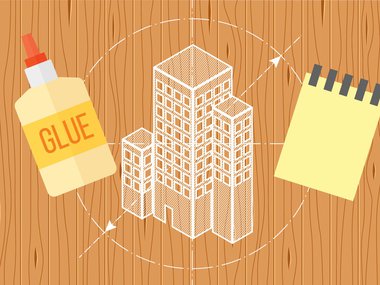 An illustration of a design for a building on top of a wooden background. Also illustrated is a glue bottle and a note pad.