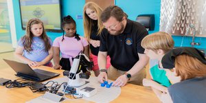 young guests surround an educator demonstrating an activity with a robotic arm.jpg