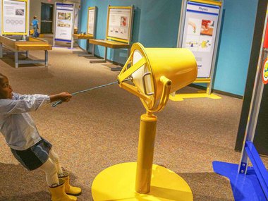 Child pulls on a yellow cannon in the exhibition Science Unplugged